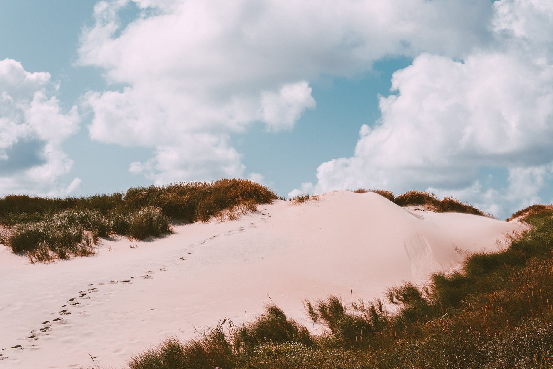 Footprints on a sanddune with blue sky and white puffy clouds. *decorative