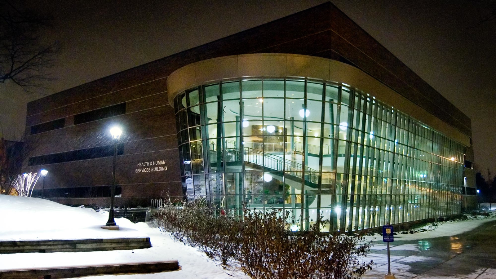 Exterior view of LCC's Health and Human Services building with lights inside, and dark outdoors.