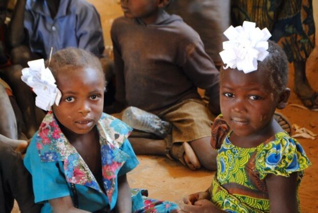 Two children in Nigeria sitting on the floor making paper flowers