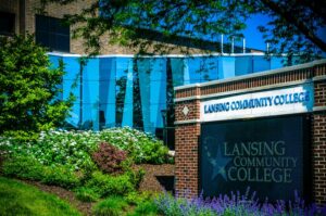 External landscape of Lansing Community College with the Arts & Science building inthe background and lush, green plantssurrounding LCC sign.