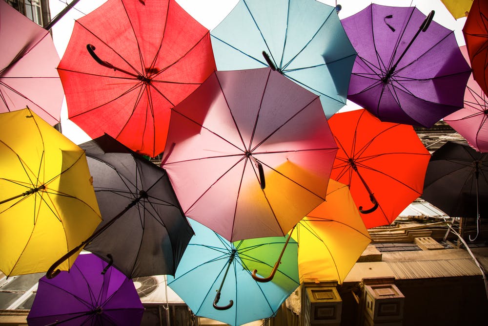 Jewel colored umbrellas haning in the sky as decor between two outdoor buildings